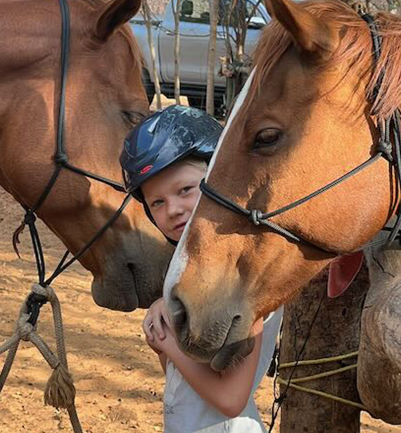 A young girl stands confidently between two horses, her eyes gleaming with pure excitement as she prepares for an outride adventure. With each horse adorned in their gear, she eagerly anticipates the journey ahead, her joy radiating from within. In this moment, amidst the bustle of preparation, she embodies the spirit of adventure and the boundless possibilities that await on the open trail. A young girl stands confidently between two horses, her eyes gleaming with pure excitement as she prepares for an outride adventure. With each horse adorned in their gear, she eagerly anticipates the journey ahead, her joy radiating from within. In this moment, amidst the bustle of preparation, she embodies the spirit of adventure and the boundless possibilities that await on the open trail.