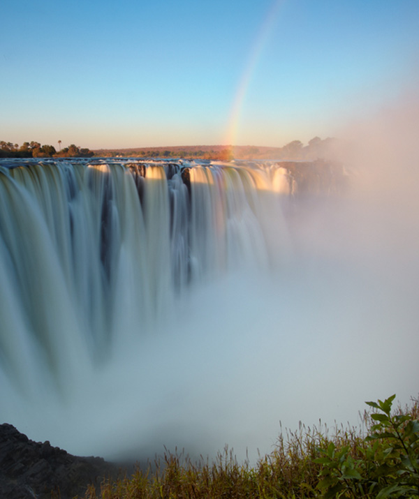 Victoria Falls, between Zambia and Zimbabwe, is a stunning sight at dawn. The rising sun bathes the rocky edge in golden light as the Zambezi River flows gracefully over, creating rainbows in the mist. It's a powerful and beautiful testament to nature's majesty. Victoria Falls, between Zambia and Zimbabwe, is a stunning sight at dawn. The rising sun bathes the rocky edge in golden light as the Zambezi River flows gracefully over, creating rainbows in the mist. It's a powerful and beautiful testament to nature's majesty.